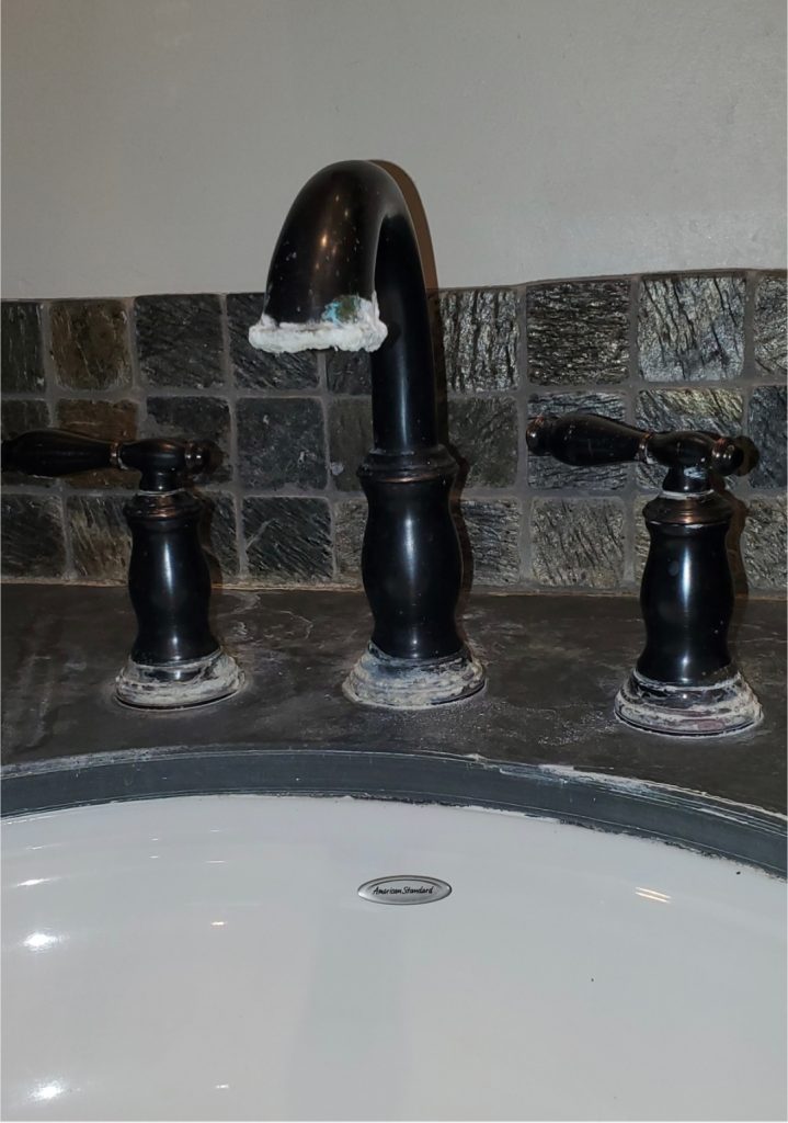 Bathroom faucet and handles with heavy hard water mineral buildup around the base of the fixtures.
