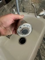 Close-up of a kitchen faucet spray head covered with heavy hard water mineral deposits, showing calcium and magnesium scale buildup caused by untreated water.